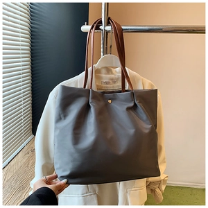 Detail of dark gray waterproof tote bag with brown leather handles on clothes rack