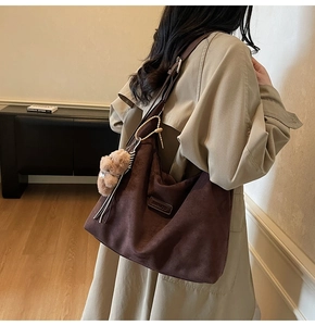 Detail of suede tote bag with brand logo and plush bear charm on the shoulder