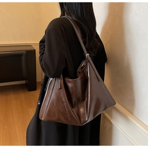 Detail of a large dark brown faux leather tote bag with glossy finish on a shoulder