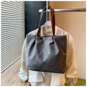 Detail of grey waterproof nylon tote bag with brown handles hanging on a white blazer