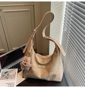 Detail of khaki suede half-moon tote with adjustable strap and plush puppy charm