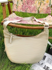 Minimalist beige crescent shoulder bag with pleated texture and wide strap on lawn