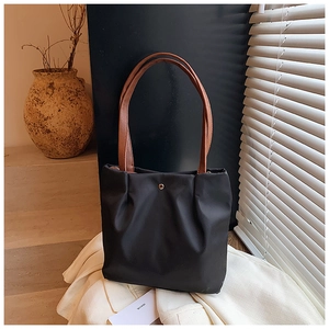 Detail of black pleated nylon tote bag with brown faux leather handles and gold buckle