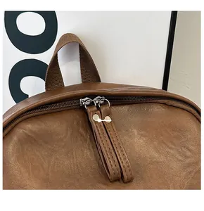 Detail view of smooth dual metal zippers and brown fabric handle on a vintage backpack