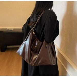Detail of dark brown leather tote bag showing glossy texture and slim shoulder straps