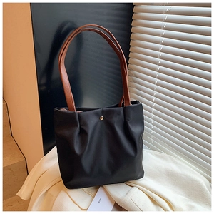Detail of minimalist black nylon tote bag featuring a gold buckle and brown leather strap