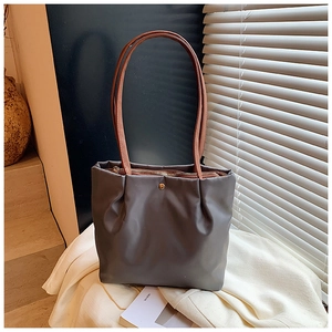 Detail view of grey pleated tote bag with golden snap button and long brown shoulder strap