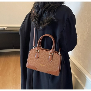 Detail of a brown leather handbag with leopard print sides and adjustable strap on a model