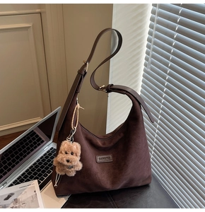 Detail of suede tote bag with plush puppy charm and adjustable strap on a cozy desk