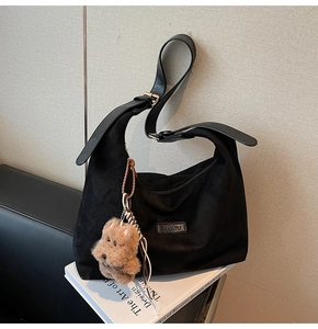 Detail of black suede tote bag with adjustable wide strap and brown teddy bear charm