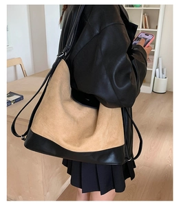 Detail of a large hobo bag in mustard suede and black leather on a model's shoulder
