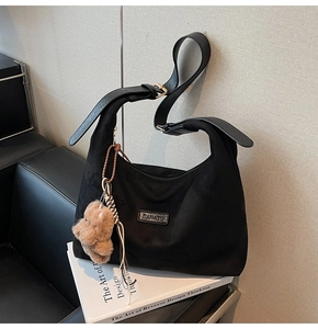 Detail of black suede Hobo bag on leather sofa with cute brown teddy bear pendant