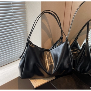 Detail of a black glossy hobo bag with thin shoulder straps on a sunlit table