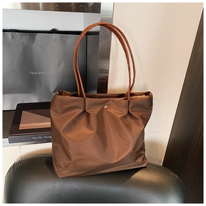 Detail of a dark brown nylon tote bag with pleated design and elegant gold metal snap button