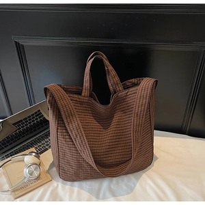 Detail of large brown plaid canvas tote bag with shoulder strap in a cozy desk setting