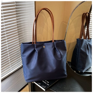 Detail of navy nylon tote bag showing gold metal snap button and leather shoulder straps