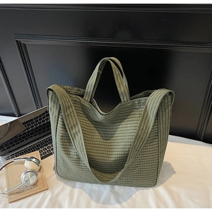 Close-up of green checkered canvas tote bag with laptop and headphones on a desk