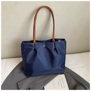 Detail of navy nylon tote bag featuring brown leather handles and golden metal buckle