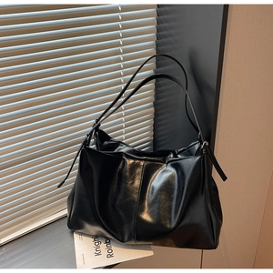 Detail view of glossy black faux leather tote bag with soft pleats and slim strap