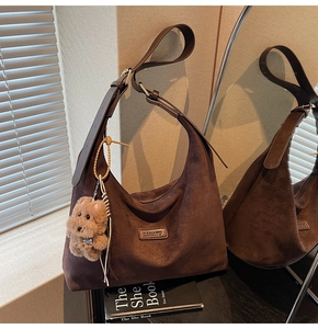 Close-up of brown suede hobo bag with adjustable strap and plush dog accessory