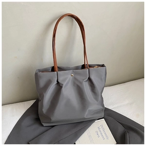 Detail of grey nylon tote bag featuring gold button closure and brown leather straps