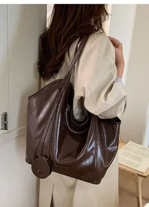 Deep brown glossy leather tote bag with round pendant shown on a shoulder in daily use