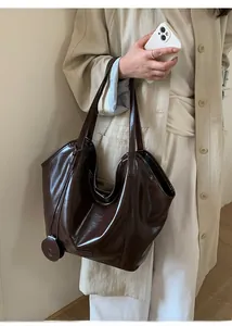 Detail view of large dark brown polished leather tote bag with long handles and charm