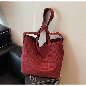 Detail view of large canvas tote bag with red and black plaid pattern in a lifestyle setting
