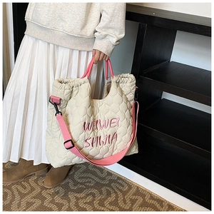 Close-up of quilted heart patterns and embroidered logo on off-white tote bag