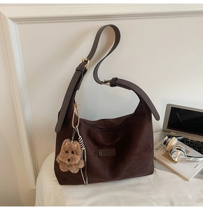 Detail of dark coffee suede hobo bag featuring a cute plush bear charm and metallic logo