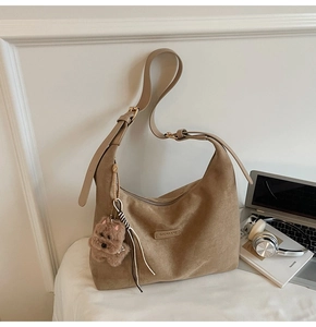 Detail of tan suede hobo bag featuring adjustable strap and plush dog charm accessory