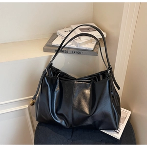 Detail of a black textured leather tote bag with silver buckle and soft pleated design