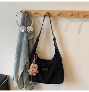 Detail of black crescent tote bag with brand patch and a cute brown teddy bear charm