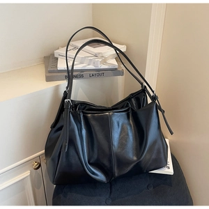 Detail of minimalist black leather tote bag with silver buckle and vertical stitching