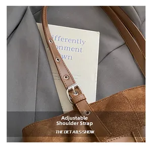 Detail of adjustable brown leather shoulder strap with silver buckle on a suede tote bag