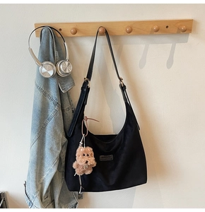 Detail of black crescent suede tote bag with puppy charm on a wooden hanger