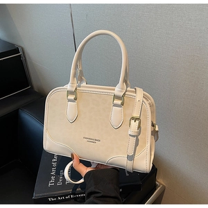 Detail of a minimalist cream leather crossbody bag with lychee grain texture and metal buckles