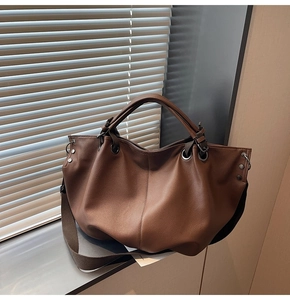 Détail du cabas en cuir marron foncé avec poignées en métal et détails de rivets