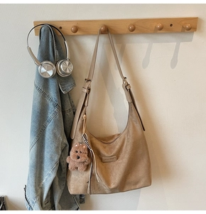 Close-up of khaki suede tote bag with cute plush puppy charm and metal brand plate