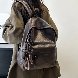 Detail of vintage brown leather backpack worn by model with elephant charm and brand logo