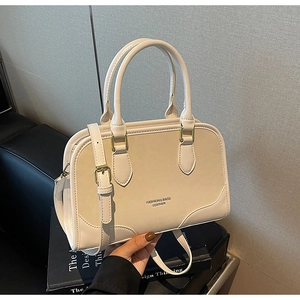 Detail of off-white leather handbag with round handles and metal buckle on book background