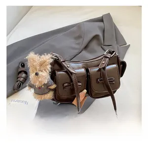 Detail of a brown leather armpit bag with multiple pockets and a plush dog charm