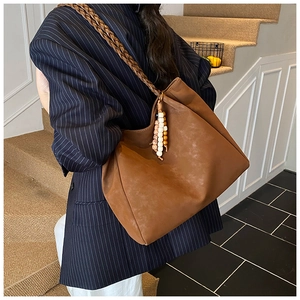 Detail of vintage brown tote bag featuring braided shoulder straps and ethnic bead charm