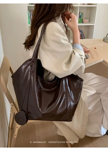 Detail of dark brown leather tote bag with a circular charm and minimalist retro design