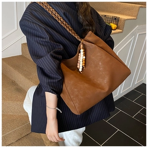 Detailed view of brown suede tote bag with woven shoulder strap and beaded tassel decor