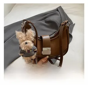 Detailed shot of brown crescent bag with a cute puppy plush charm and metal clasp closure