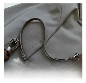 Close-up of a brown leather handbag handle with a cute white puppy plush charm detail