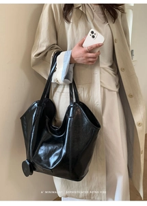 Detailed side view of the large black glossy leather tote bag carried by a model