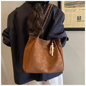 Detail of vintage brown tote bag with woven shoulder strap and wooden bead charm on a model