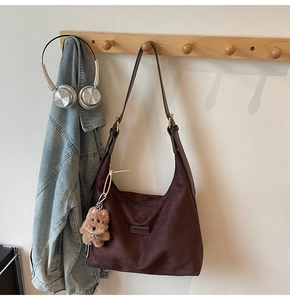 Detail of dark brown suede hobo bag with a dog plush charm and logo plaque on a wooden hanger
